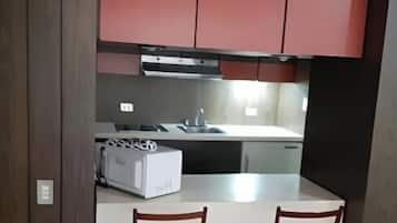 Een kleine keuken met rode kastjes, een wit aanrecht en twee houten stoelen.
