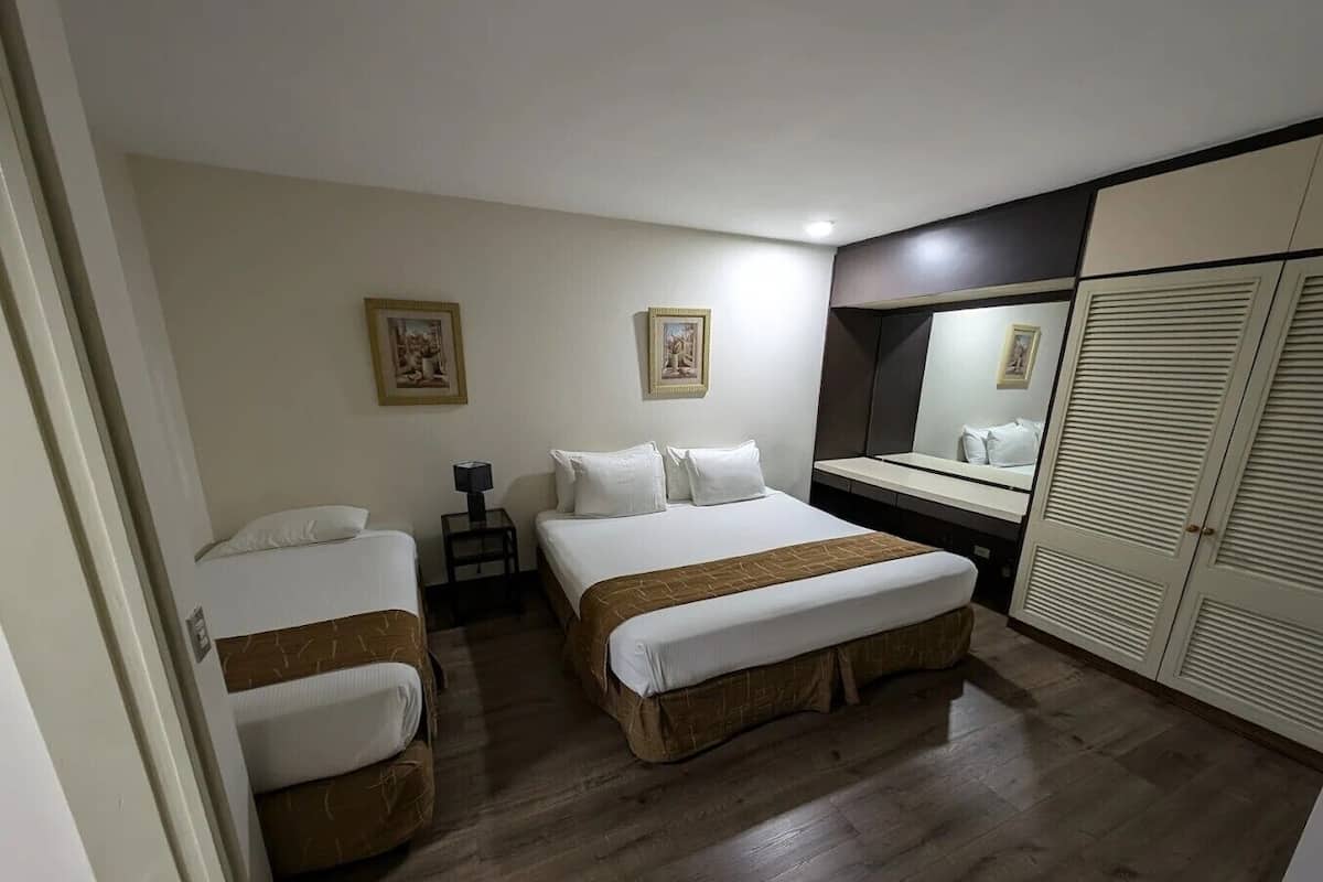 Una habitación de hotel con dos camas, un escritorio, un espejo y un armario.