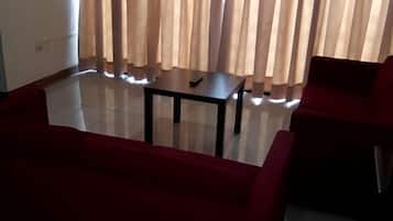 A living room with a red sofa, a small table, and a TV mounted on the wall.