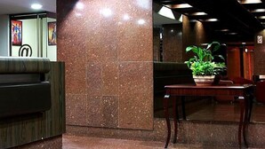 A reception area with a marble wall, a reception desk, and a potted plant on a wooden table. - Hotel Cuarta Avenida (Caracas)