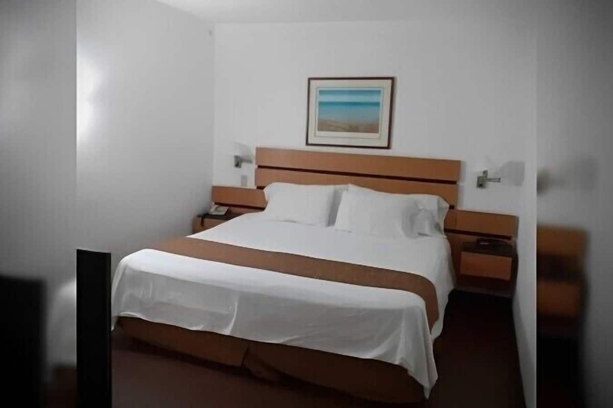 Habitación de hotel con una cama individual, una mesita de noche, una lámpara fijada a la pared y un cuadro enmarcado.