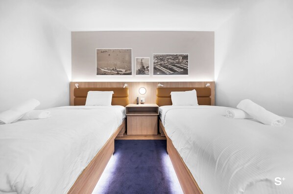 Une chambre d’hôtel avec deux lits, une petite table et une lampe fixée au mur.