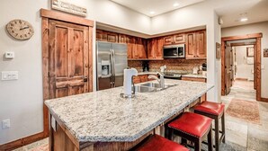 A kitchen with wooden cabinets, a stainless steel refrigerator, a granite countertop, and red bar stools. - Ski-in 2 Bedroom Townhome at Mountain Thunder (Breckenridge)