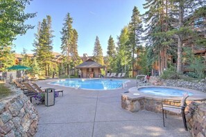 A pool area with lounge chairs, a hot tub, and a building with a thatched roof.