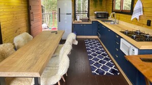 Interior de una cabaña de madera con una mesa de comedor, sillas, un refrigerador, una estufa y una ventana.
