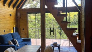 Interior de madera con sofá, mesa de comedor y sillas. Una escalera conduce a una terraza exterior.