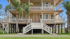 A two-story house with a balcony on the upper floor, a front porch, and a staircase leading to the entrance. - Magnolia Cottage R7 (Lafitte)