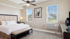 A hotel room with a bed, a ceiling fan, two windows, a framed picture, and a desk with a lamp. - Magnolia Cottage R4 (Lafitte)