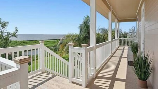 A covered balcony with white railings, a view of the ocean, and a potted plant. - Magnolia Cottage R2 (Lafitte)