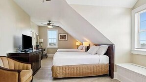 A bedroom with a bed, a desk with a TV, a chair, a ceiling fan, and a window. - Oak Cottage R302 (Lafitte)