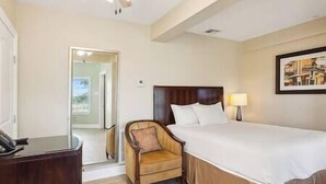 A hotel room with a bed, a chair, a desk, and a door leading to another room. - Oak Cottage R103 (Lafitte)