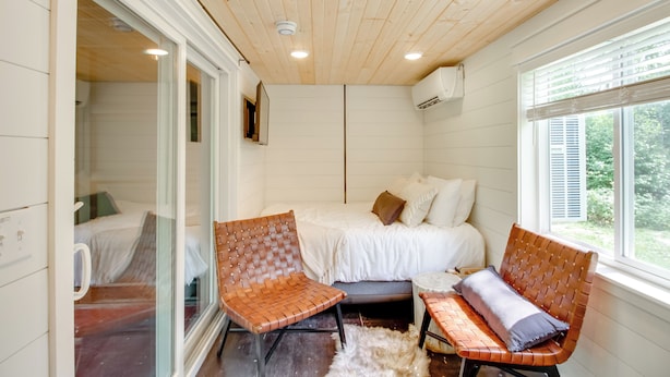Une chambre à coucher avec un lit, deux fauteuils en osier, une petite table ronde et une fenêtre avec des stores.