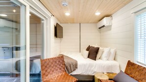 Un dormitorio con una cama, dos sillas tejidas, una pequeña mesa de madera y un televisor montado en la pared.