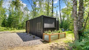 A modern cabin with a large window, surrounded by a forest. - On-Site Ice Fishing: Nashwauk Vacation Rental! (Nashwauk)