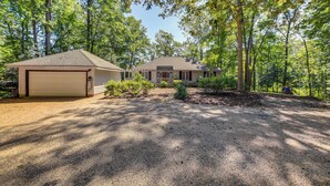 A single-story house with a garage, surrounded by trees and a gravel driveway. - Waterfront Urbanna Home w/ Private Dock (Urbanna)