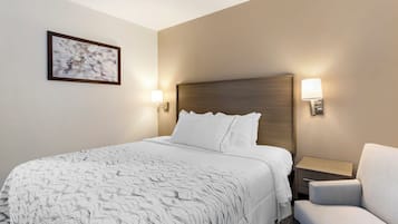 Una habitación de hotel con una cama, una silla y dos lámparas fijadas a la pared.