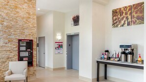 Een hotel lobby met een stenen muur, een receptiebalie, een koffieapparaat en een zithoek.