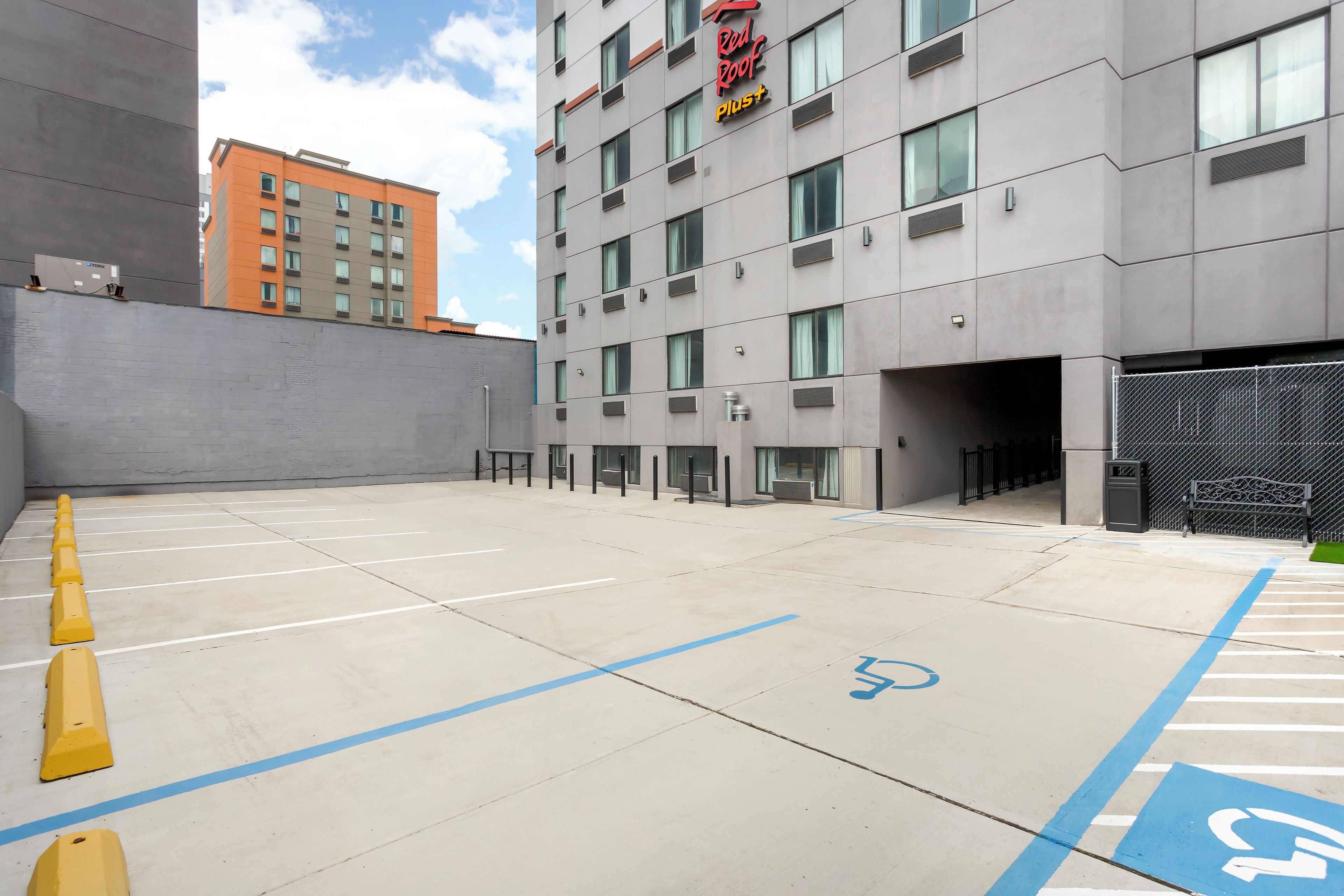 A parking area with marked spaces, a wheelchair-accessible spot, and a building with a sign reading 'Red Roof Plus'.