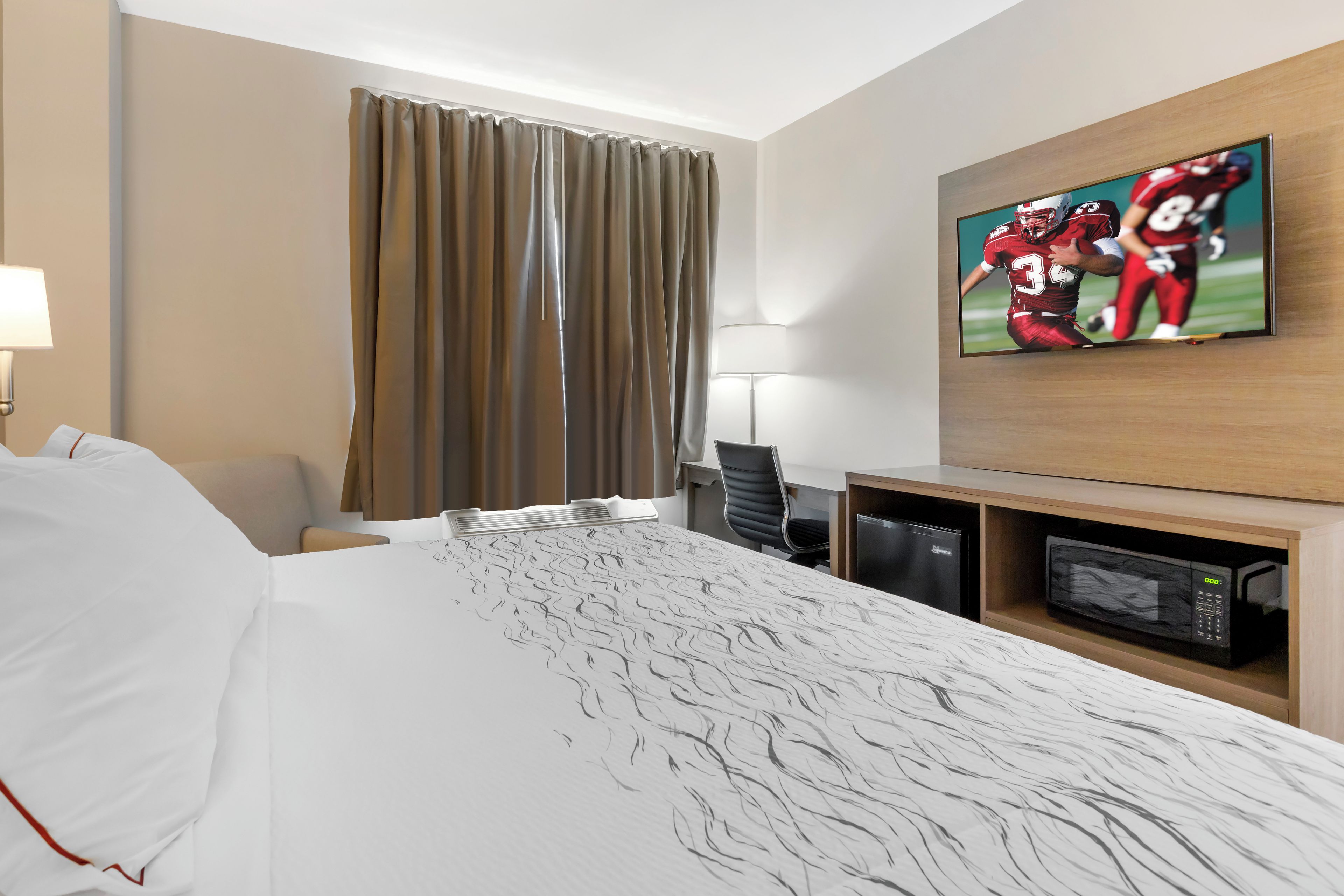 A hotel room with a bed, a desk with a computer, a television, and a microwave.
