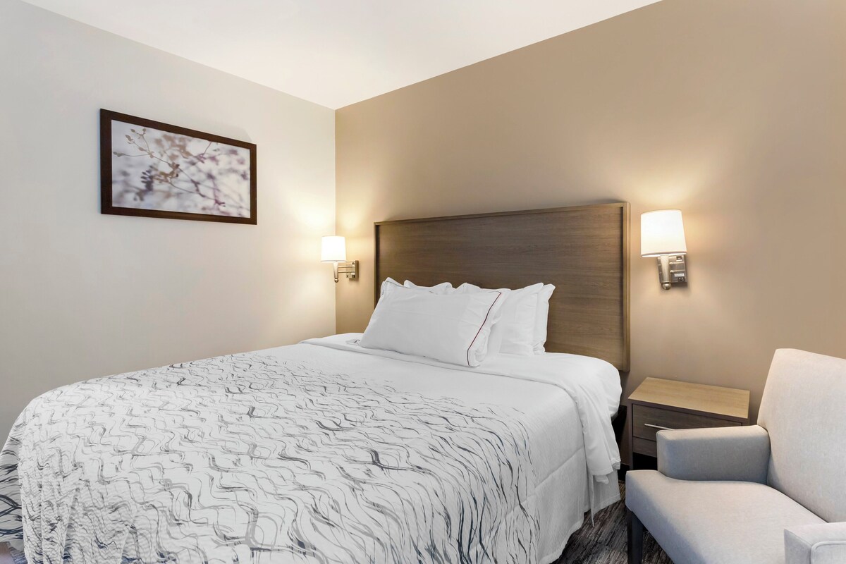 Une chambre d’hôtel avec un grand lit, deux tables de chevet, une chaise et une œuvre d’art accrochée au mur.