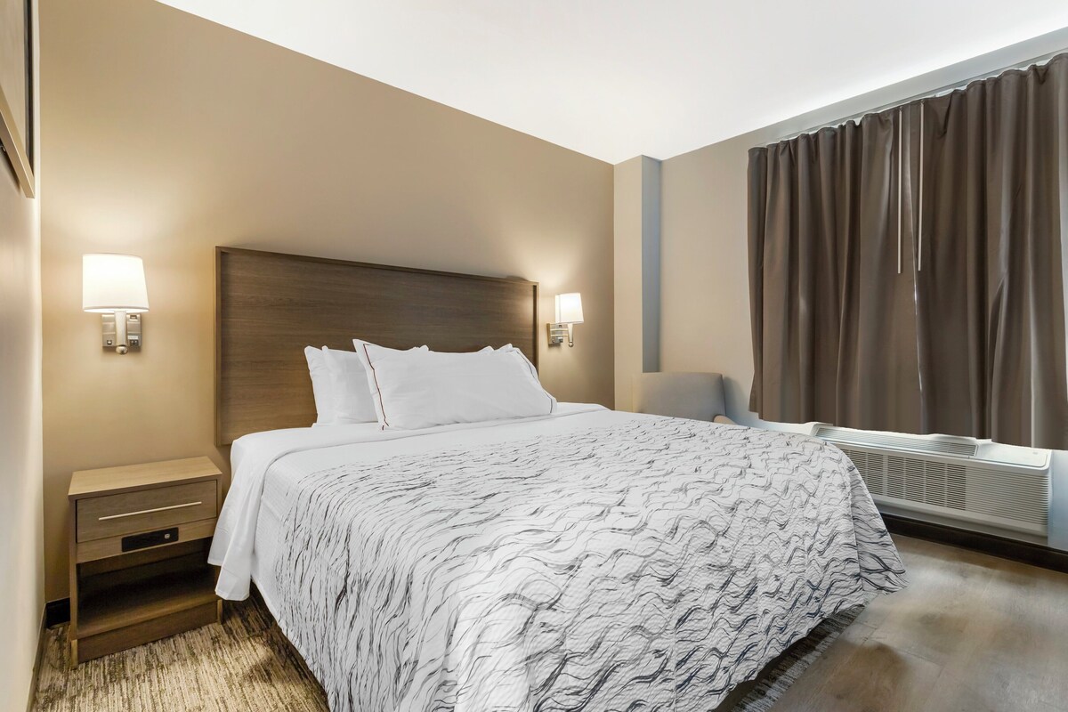 Une chambre d’hôtel avec un grand lit, deux lampes de chevet, une table de chevet, une fenêtre avec des rideaux et un radiateur fixé au mur.