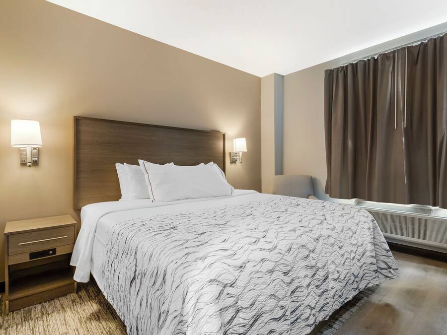 Una habitación de hotel con una cama grande, lámparas de noche, una mesita de noche, una ventana con cortinas y un calefactor de pared.