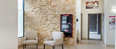 A hallway with a stone wall, two chairs, a fire alarm command center, and a door leading to another room.