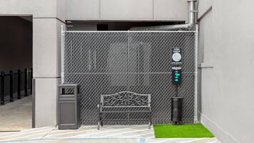 Uma entrada gradeada com cerca de metal, um banco, uma lata de lixo e uma placa instruindo a recolher os dejetos de animais de estimação.
