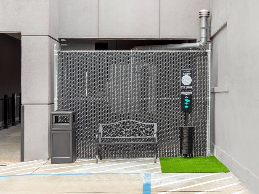 A gated entrance with a metal fence, a bench, a trash can, and a sign instructing to clean up after pets.