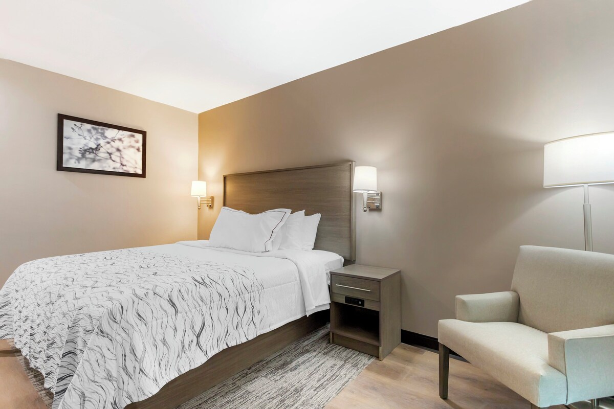 Une chambre d’hôtel comprenant un lit, une table de chevet, une chaise et une lampe fixée au mur.