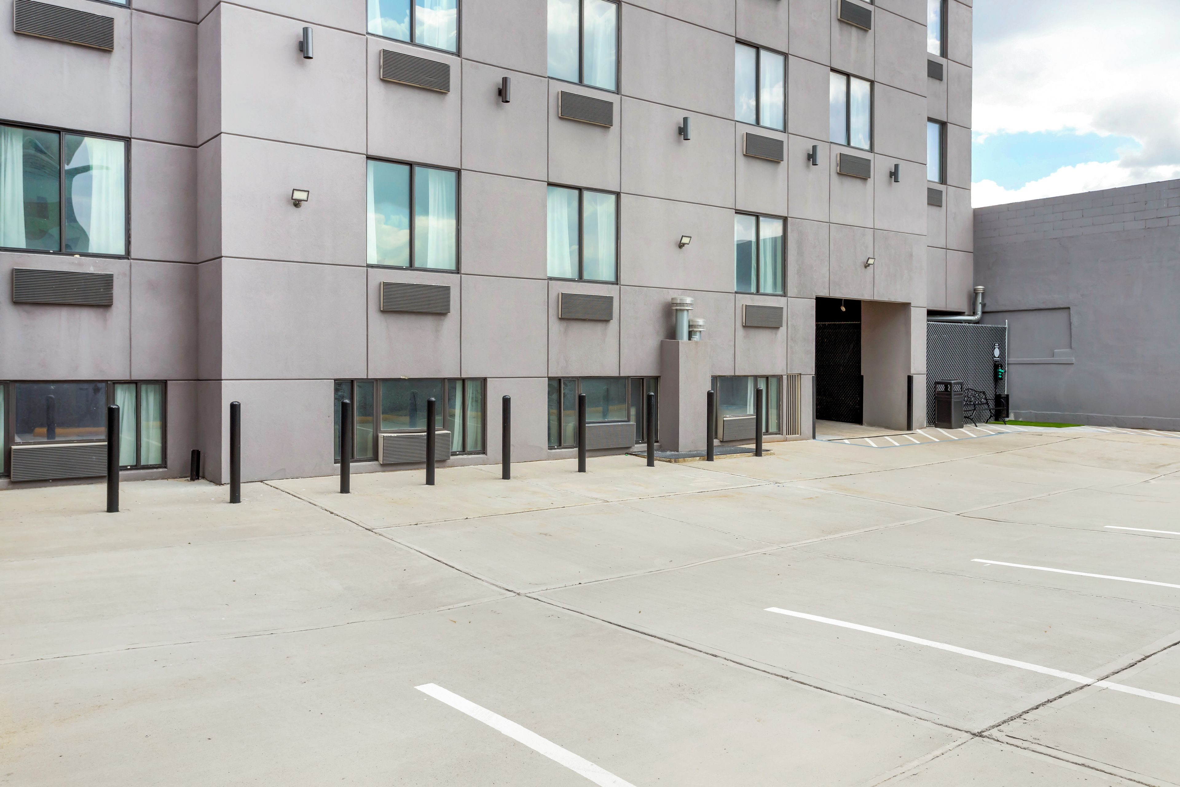 A modern building with a flat facade, multiple windows, and a parking area with marked spaces.