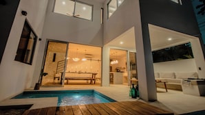 Et moderne hus i to etager med swimmingpool, spiseområde og en stue med sofa og sofabord.