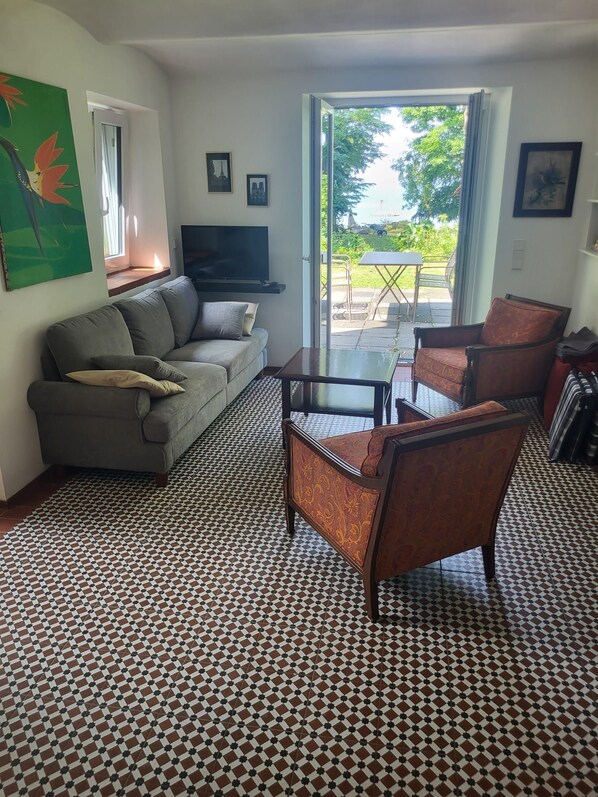A living room with a sofa, armchairs, a coffee table, a flat-screen TV, and a patterned floor.