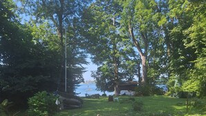 An outdoor dining area with a table set for four, surrounded by chairs, set against a backdrop of trees and a view of the water.