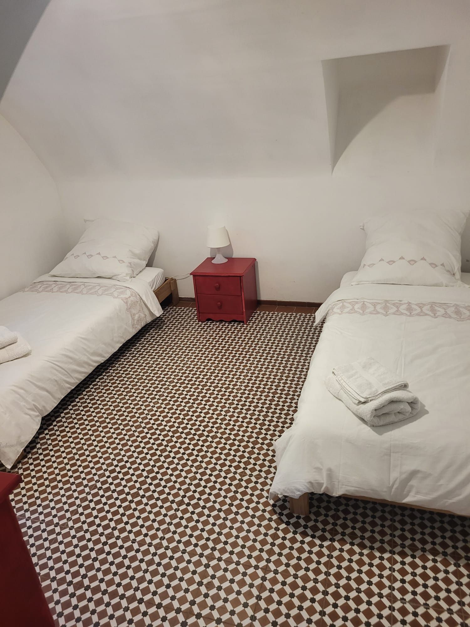Une chambre avec deux lits, une table de chevet rouge et un sol à motifs.