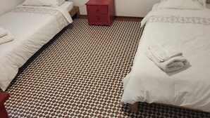A room with two beds, a red nightstand, and a patterned floor.
