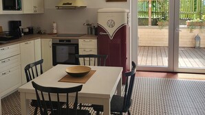 A compact kitchen with white cabinets, a microwave, a stove, and a red refrigerator. There is a dining table with chairs and a bowl on it. The floor has a patterned tile design.