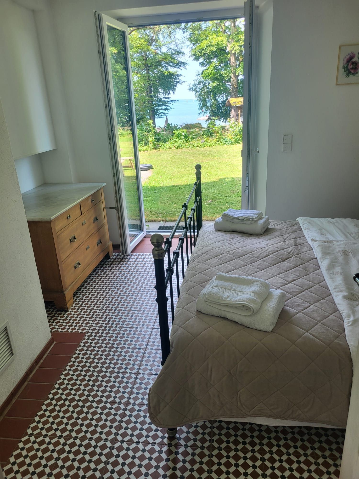 A bedroom with a bed, a dresser, and a view of a garden through an open door.