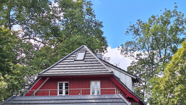 A red house with a balcony, a front door, and a staircase leading to the entrance.