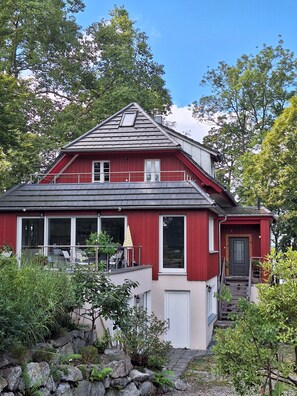 A red house with a balcony, a front door, and a staircase leading to the entrance.