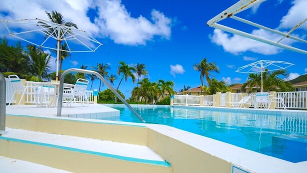 Un espace piscine avec des marches menant à l’eau, des chaises longues et des parasols.