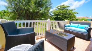 Un balcon doté de mobilier en osier, comprenant des chaises et un canapé, ainsi qu’une balustrade blanche.