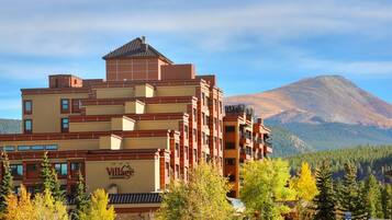 Un hotel de varios pisos con un letrero grande de Village, rodeado de árboles y una montaña al fondo.
