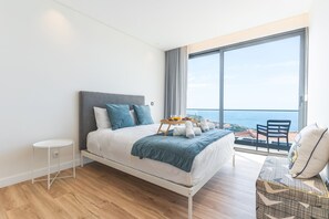 A modern bedroom with a bed, a small side table, a balcony with a view of the sea, and a chair. - Sapphire Sands by Atlantic Holiday (Calheta)
