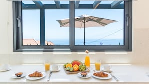 A breakfast setup with croissants, fruits, and juice on a kitchen counter, overlooking a scenic view through a window. - Sapphire Sands by Atlantic Holiday (Calheta)