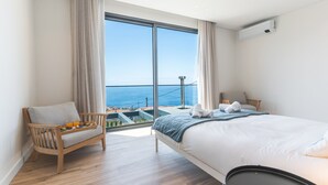 A bedroom with a large window, a bed, a chair, and a small table with fruits. - Sapphire Sands by Atlantic Holiday (Calheta)