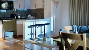 A modern kitchen with white cabinets, a microwave, a stove, and a small island with bar stools. - Estudio apartamento Juan Dolio (Guayacanes)