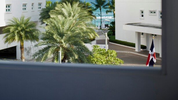 A view of a building with multiple floors and a flag in front. - Estudio apartamento Juan Dolio (Guayacanes)