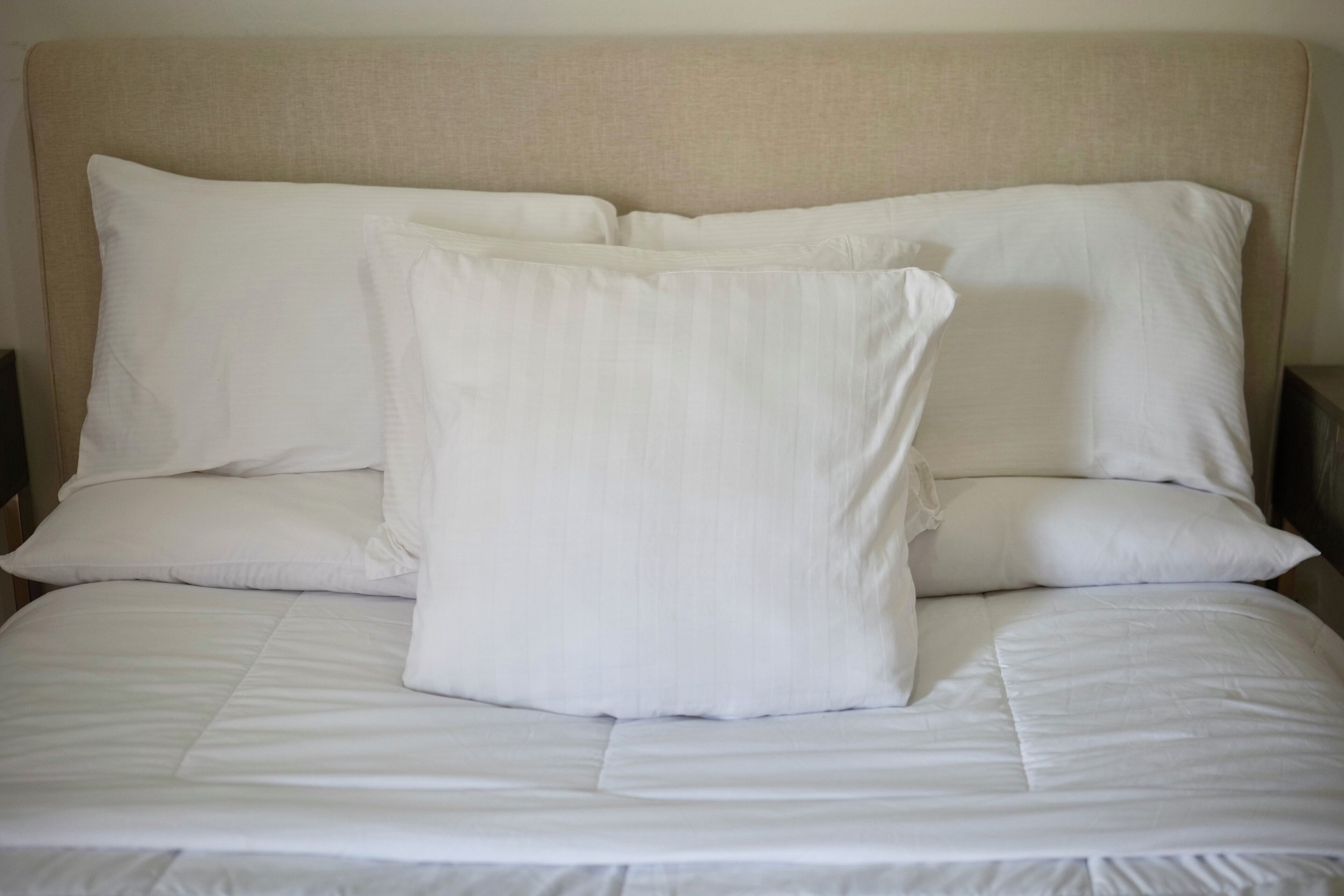Una cama con ropa de cama blanca y un cabecero color beige.