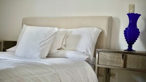 A neatly made bed with white linens and pillows, a wooden nightstand with a drawer, and a blue vase on the nightstand. - Estudio apartamento Juan Dolio (Guayacanes)
